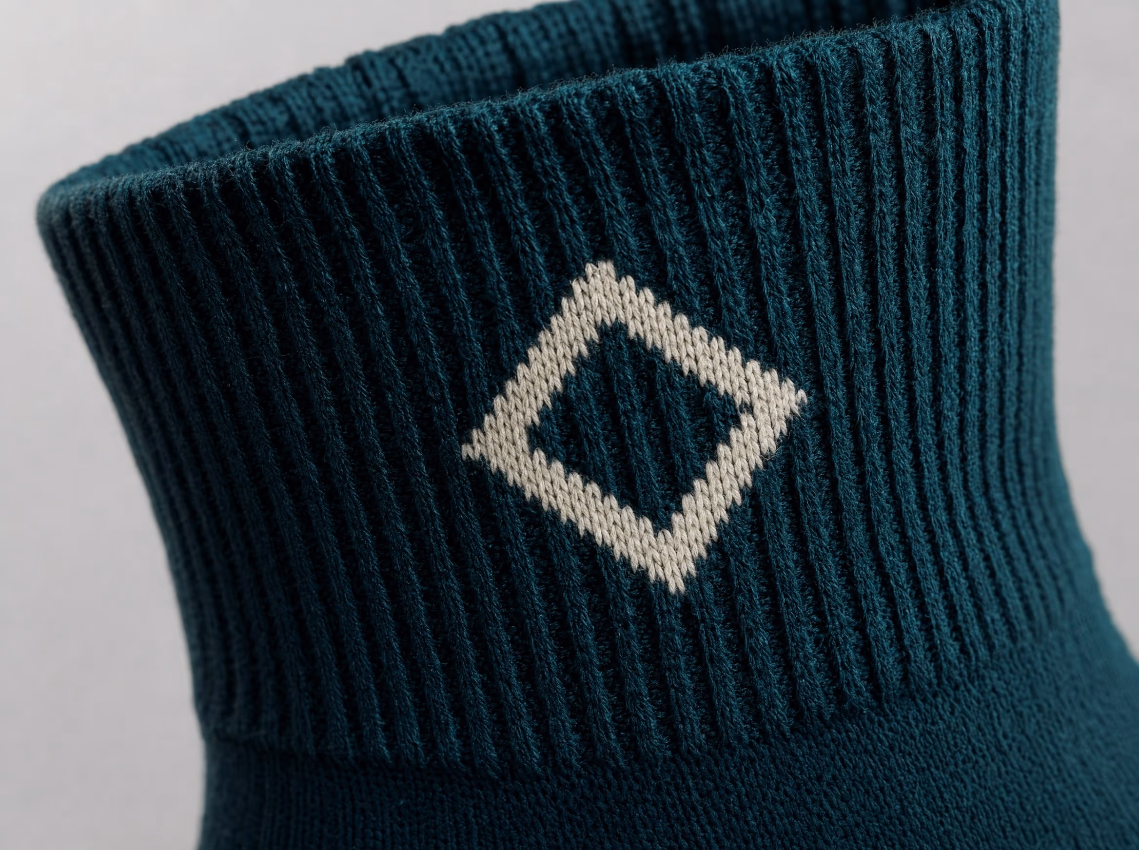 Close-up of a deep-teal sock cuff with a geometric emblem knit into the ribbing in contrasting cream yarn